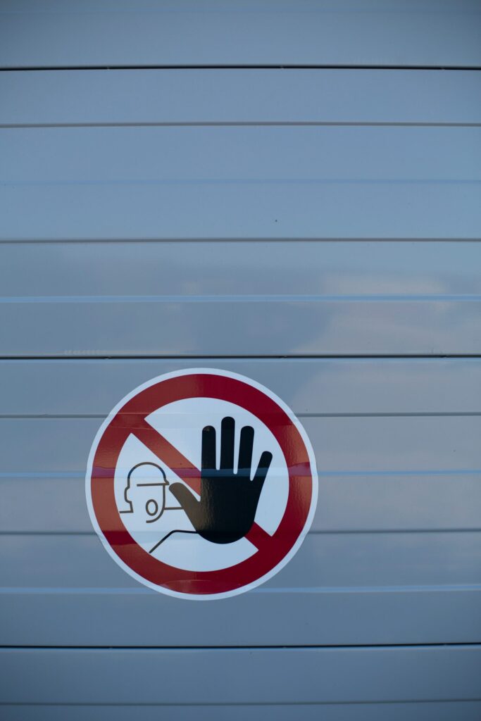 Circular red no-touch sign on a gray surface, showing a raised hand in front of a small figure—do not touch.