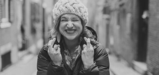 Cheerful woman in a chunky knit hat and puffer jacket, making a rock-on gesture in a blurred urban alley.