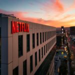 Red Netflix sign on a modern office building at sunset overlooking a busy city street, with pink-orange sky above.