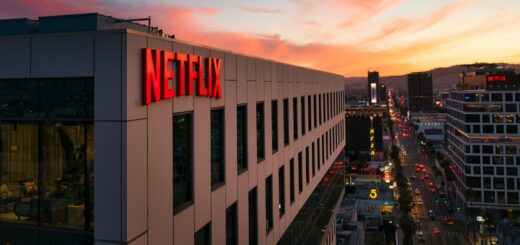 Red Netflix sign on a modern office building at sunset overlooking a busy city street, with pink-orange sky above.