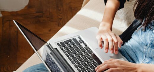 Person sits on a beige couch and types on a laptop resting on their lap in a home setting.