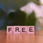 Four pink Scrabble tiles on a wooden table spell 'FREE', with a soft-focus background.